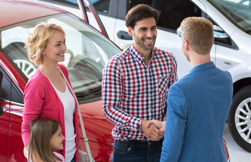Family at car dealership, man shaking hands with sales person