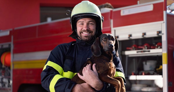Firefighter in uniform standing in front of fire truck holding a dog