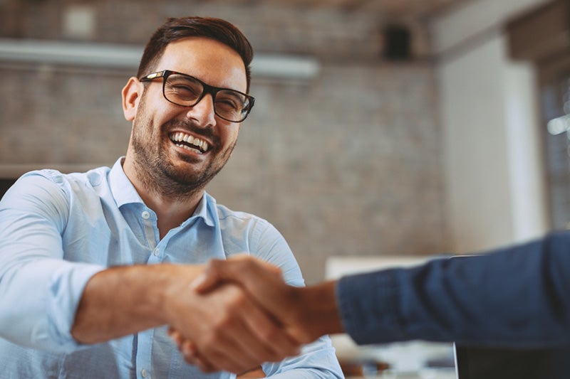 Man smiling shaking hands with another person 