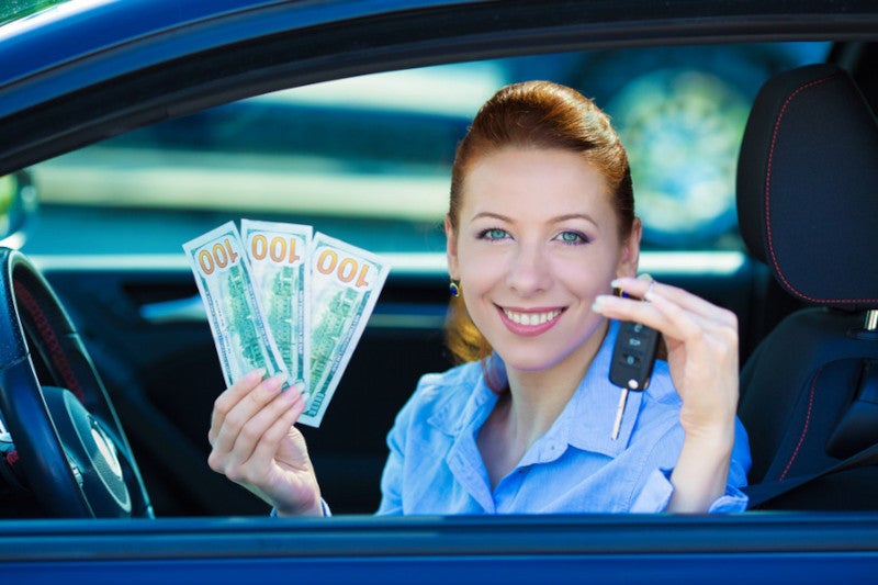 Woman in driver's seat showing off cash and car key