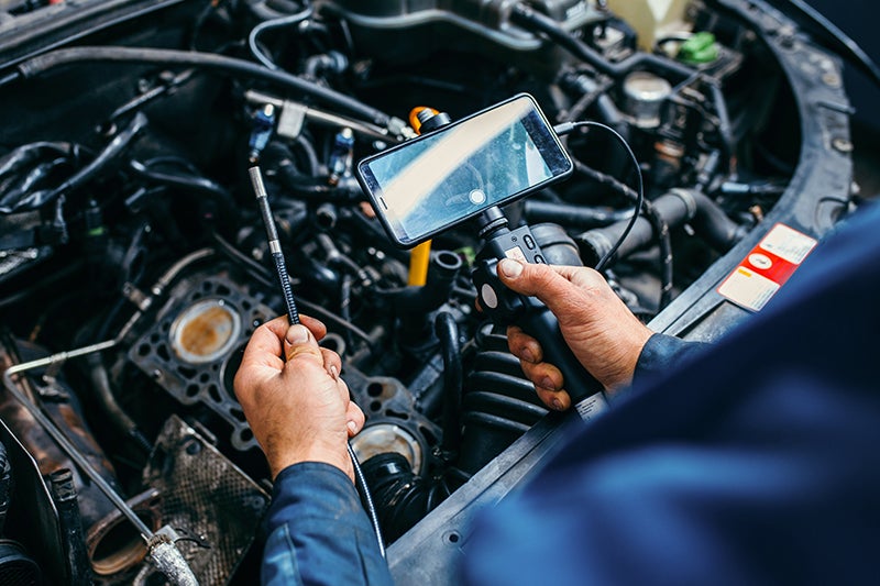 Technician performing inspection on car engine with electronic testing equipment